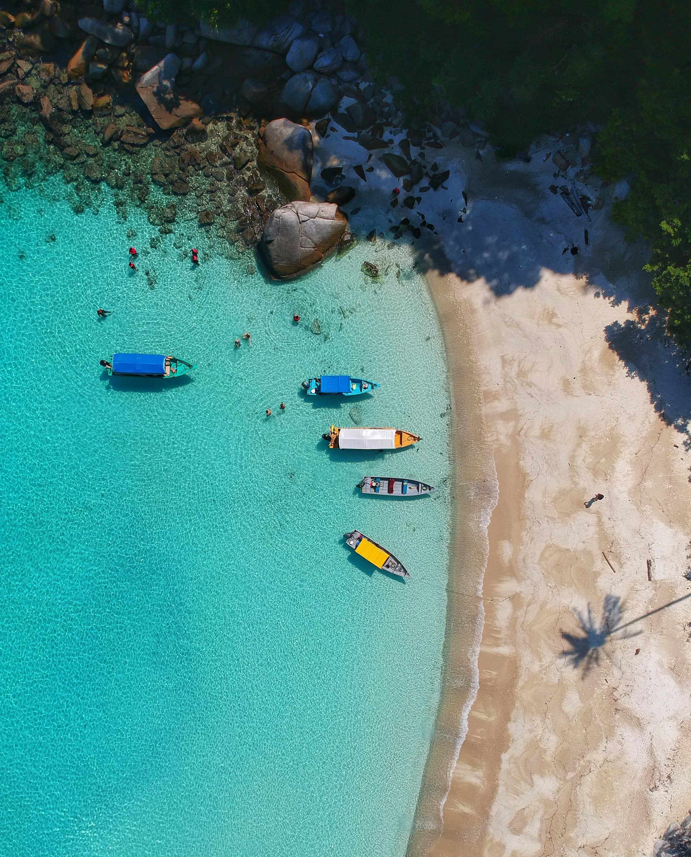 Aerial view of a turquoise cove with boats moored along a white-sand beach