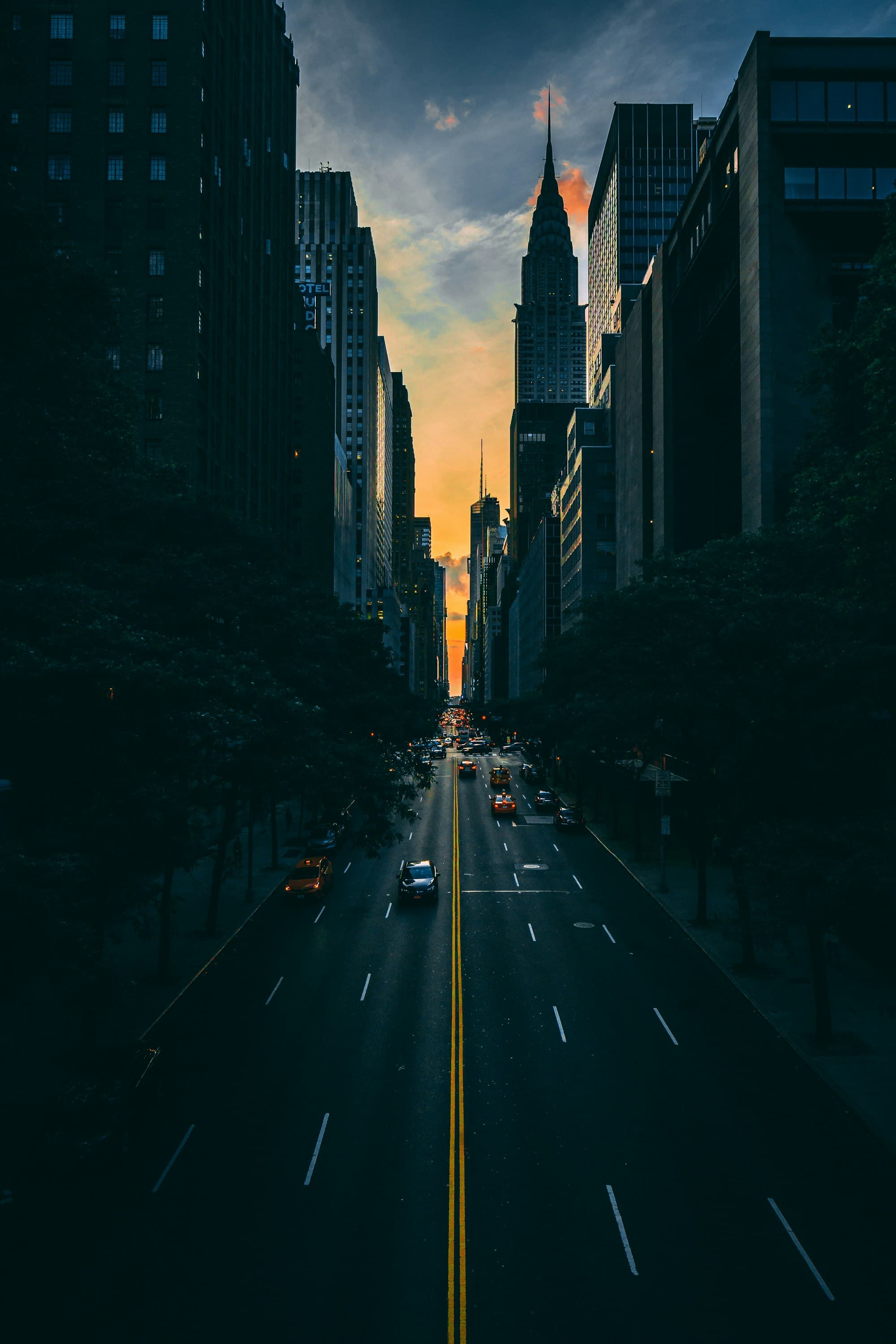 A city avenue at dusk with a glowing sunset between the buildings